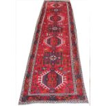 A hand woven wool Persian Heriz runner, worked with seven hooked gulls against a red ground,