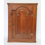 An oak hanging corner cabinet, with panelled door enclosing serpentine shelves,