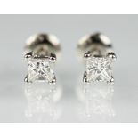 A pair of diamond stud earrings, each set with a single princess cut diamond,