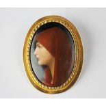 A yellow metal mounted ceramic panel mounted brooch, the panel depicting a lady in a red head scarf,