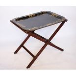 A 19th century lacquered papier mache tray on folding stand,