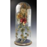 A Victorian silk work, synthetic and natural grass floral display, modelled in a glass vase,