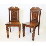 A pair of late Victorian walnut hall chairs, with carved backs and solid seats,
