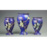 A garniture of three Carlton Ware vases, decorated with fruiting trees against a deep blue ground,