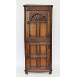 A carved oak free standing corner cabinet with arched panelled door above another door,