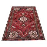 A Caucasian hand woven wool carpet, worked with a geometric design against a red ground,