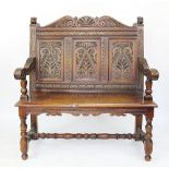 A 1920's carved oak settle, with scroll panelled back and solid seat on turned legs,