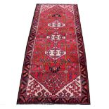 A Persian hand woven wool runner, worked with a geometric Caucasian design against a red ground,