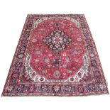 A Persian Tabriz wool carpet, worked with a geometric medallion design against a red ground,