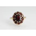 A garnet set cluster ring, the central oval garnet within a surround of ten further garnets,