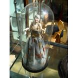 A china half doll flapper girl in cloth dress on a wooden base under a glass dome.