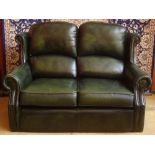 A modern two seater sofa upholstered in green leather.