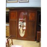 An Edwardian mahogany three door wardrobe with two internal drawers, shelving, a clothing rack, coat