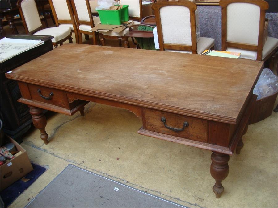 A teak 20th Century Indonesian desk, on turned legs with two drawers.