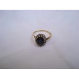An 18ct yellow gold ring (EJ, London 1973), with white gold claw set sapphire with a cluster of