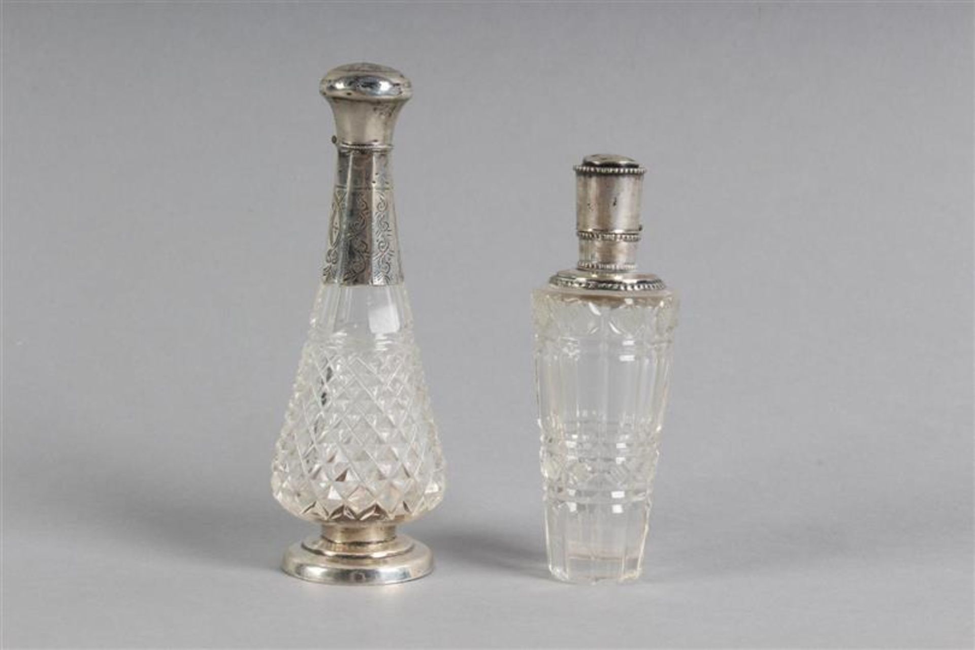 Twee parfumflesjes met zilveren dop. H: 11 en 9 cm.