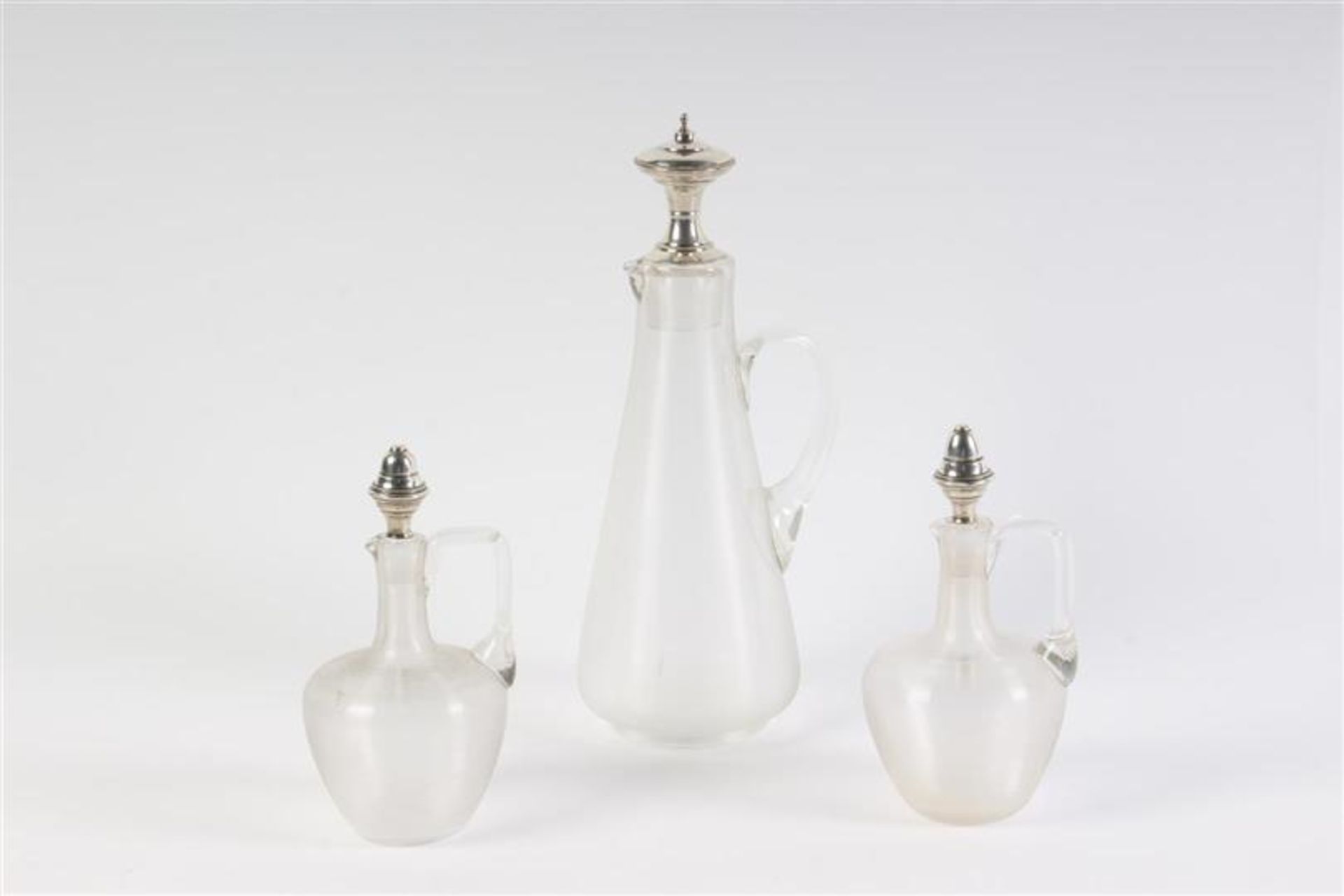 Drie karaffen van draadglas met zilver. H: 19 - 33.5 cm.