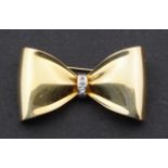 Yellow gold pin, shaped as a bow, 14 krt., set with a brilliant cut diamond, l. 3,5 cm, appr. 3.6