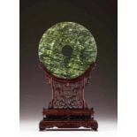 A jade disc screen with stand Polished spinach-green jade Carved and pierced wood base with floral