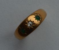 An emerald and diamond three stone gypsy set ring