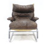 A 1970's tubular and brown upholstered armchair with exposed stitching on a slide base