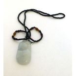 A black bead necklace suspending a pale green jade seed shaped pendant, pendant l.