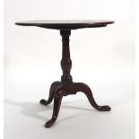 An 18th century oak tilt-top table, the circular surface on a turned column and three splayed feet,