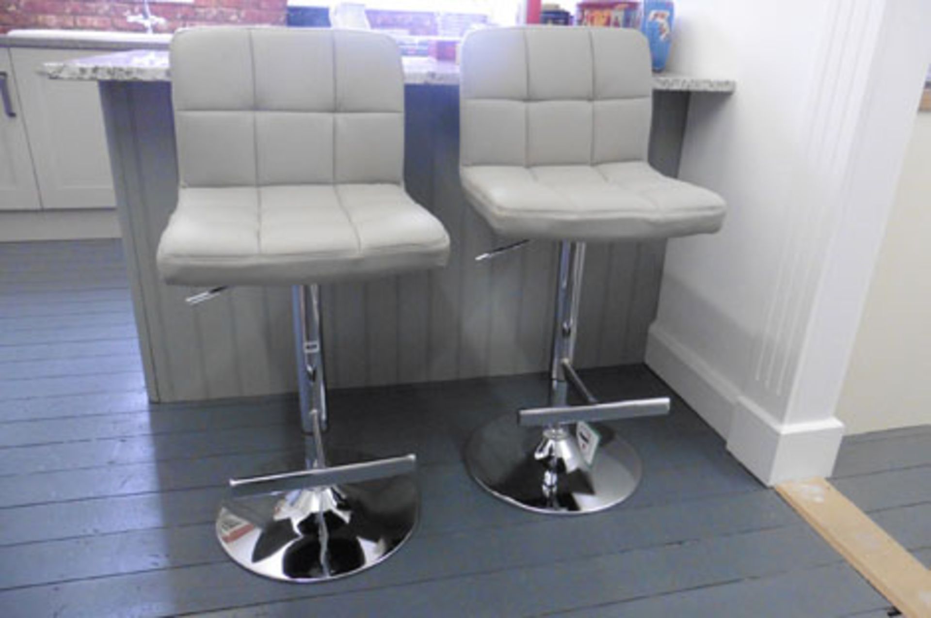 A pair of cream leather-upholstered chrome based adjustable height bar stools