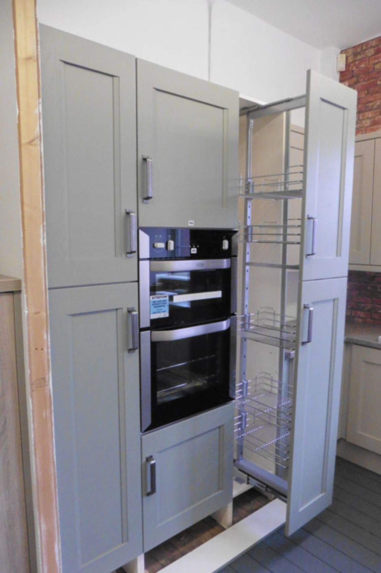 A small kitchen display in olive green finish in a shaker-style, with a pull-out larder cupboard (