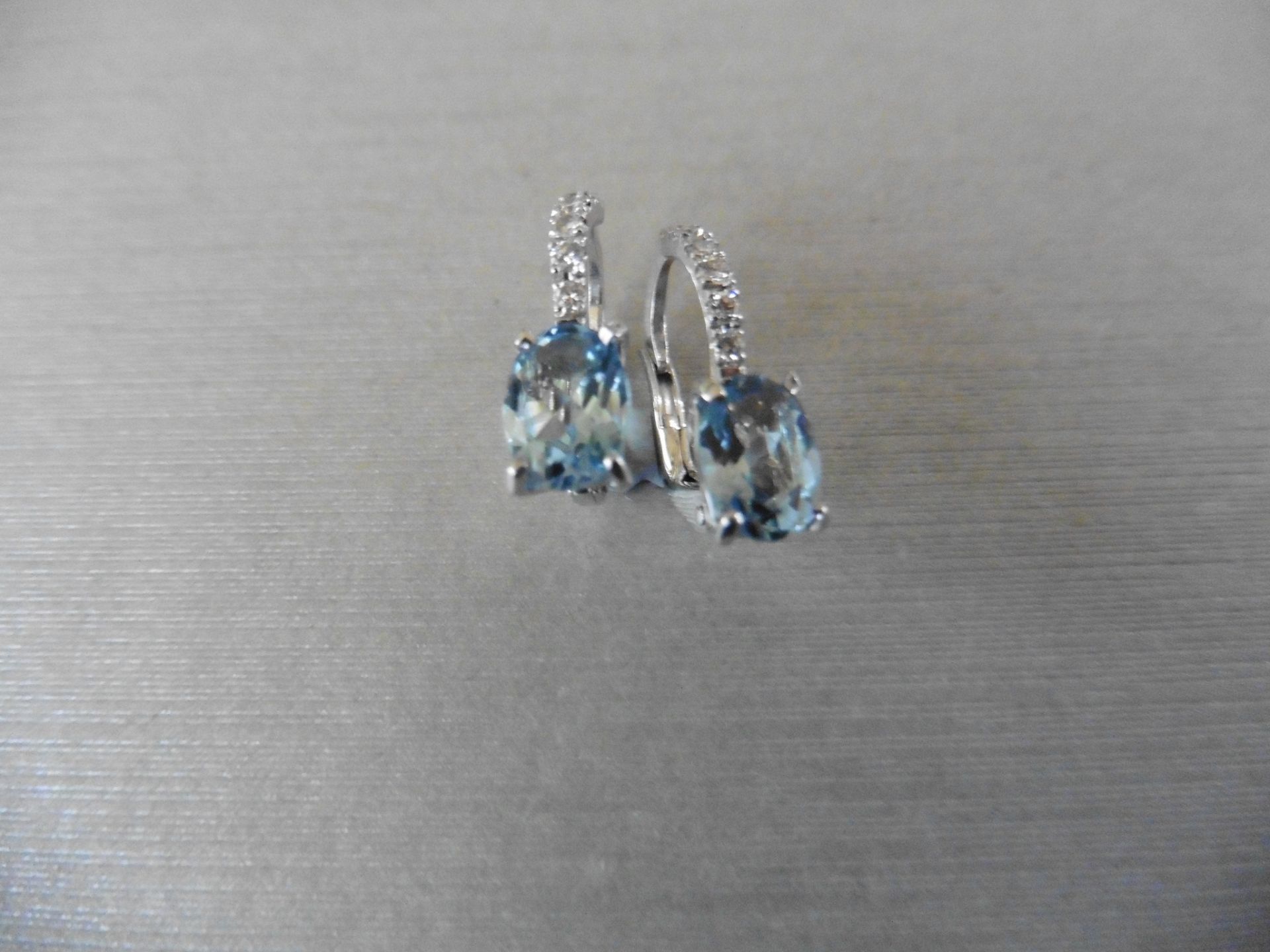 1.60ct Aqua marine and diamond hoop style earrings. Each is set with a 7x 5mm oval cut aqua with 6