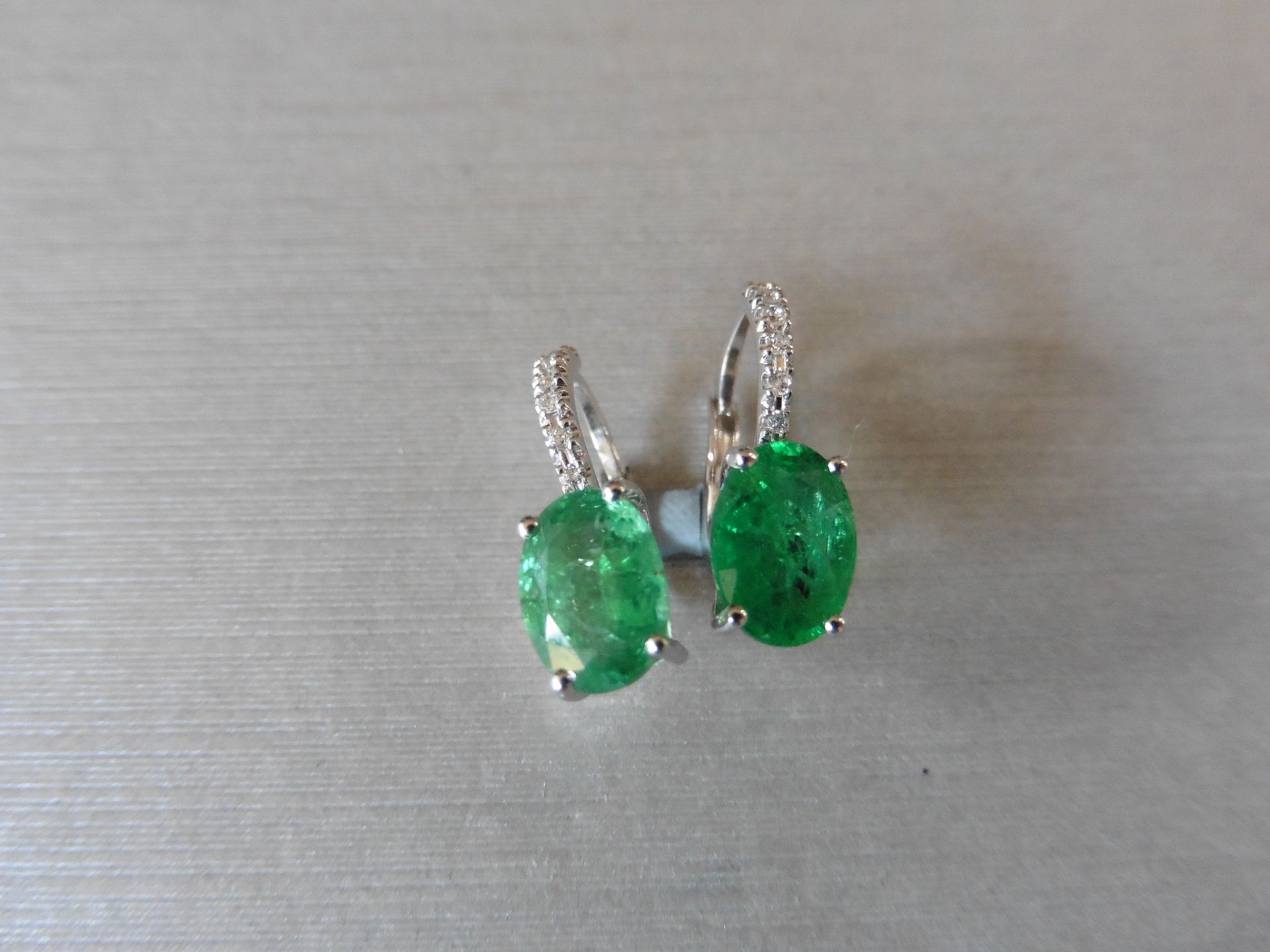 1.60ct emerald and diamond hoop style earrings. Each is set with a 7 x 5mm oval cut emerald with 6