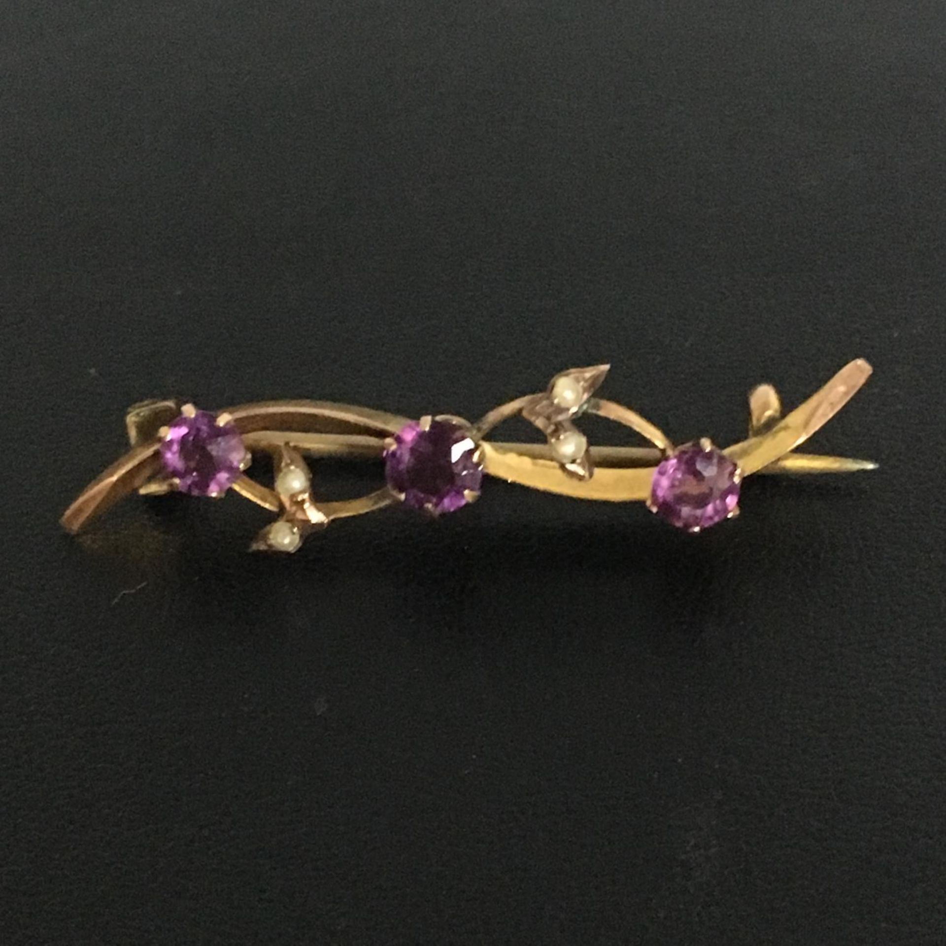 9CT GOLD AMETHYST AND SEED PEARL BAR BROOCH. In a wave design with a "c" clasp. The hammer price