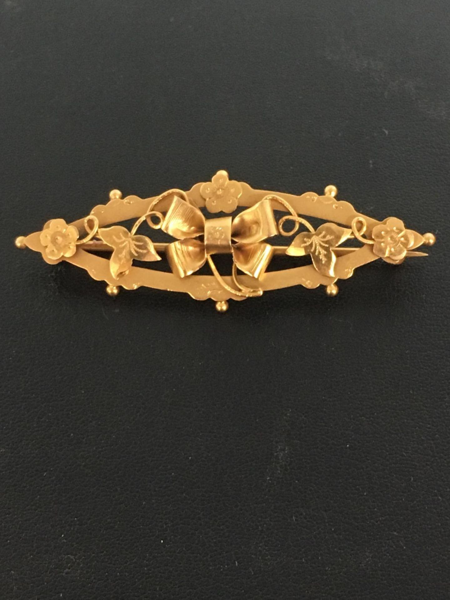 9CT GOLD BOW DESIGN BAR BROOCH. With leaves and flowers. The hammer price includes free packing &