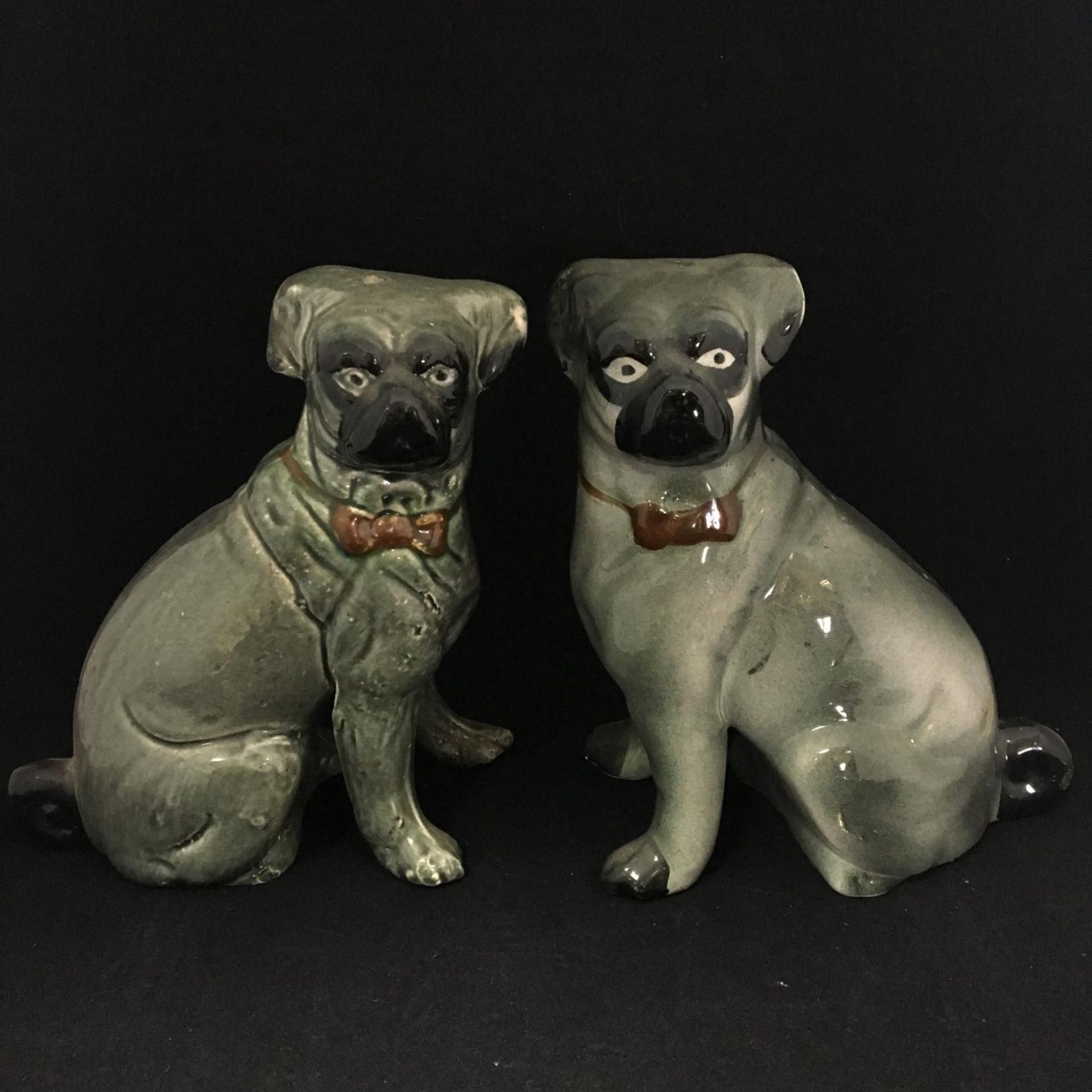Antique Victorian era ceramic seated pugs. Matched (not an exact pair). Standing around 20cm high.