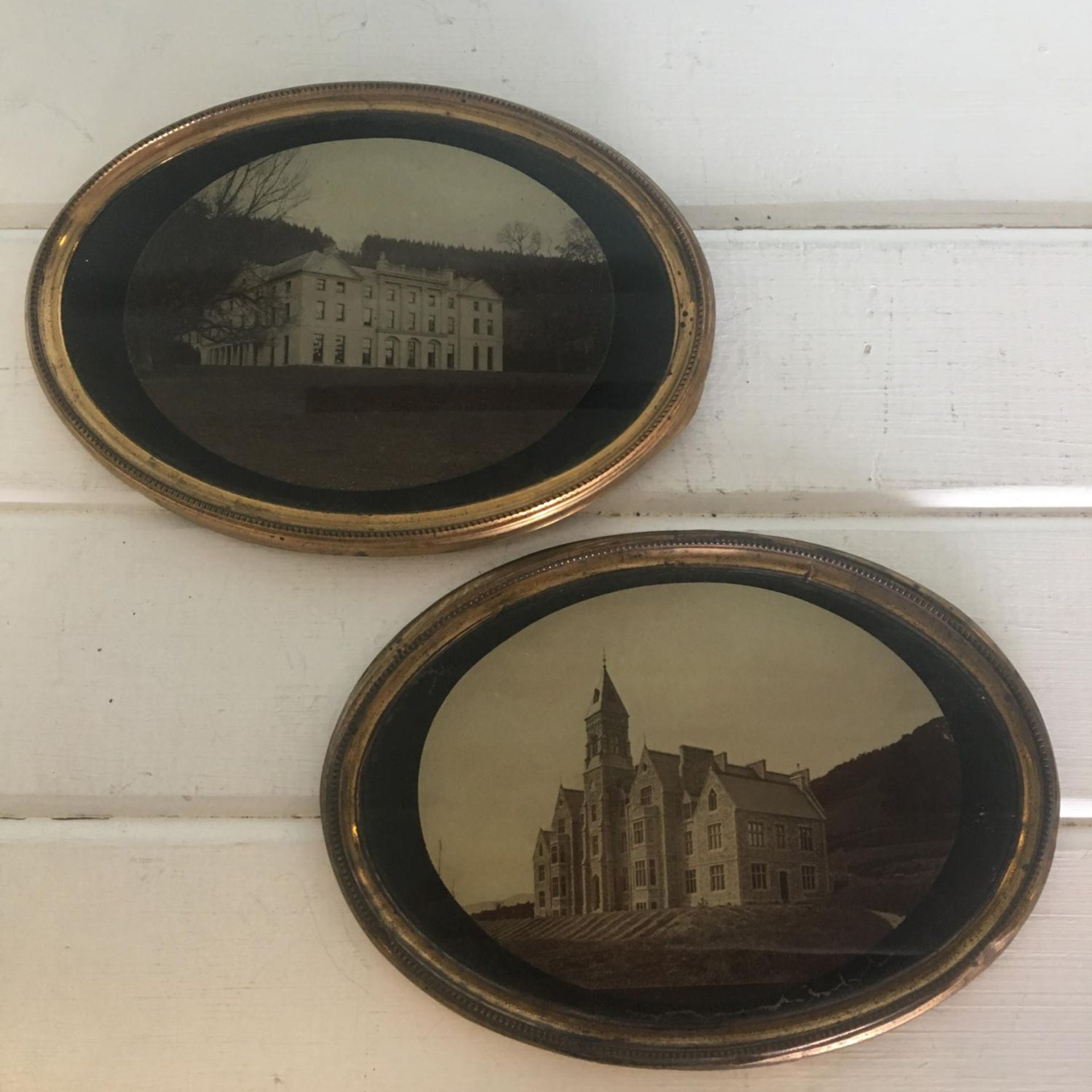 Pair of painted glass backed photographs of oval shape in gilt metal frames measuring 16cm x 12cm.