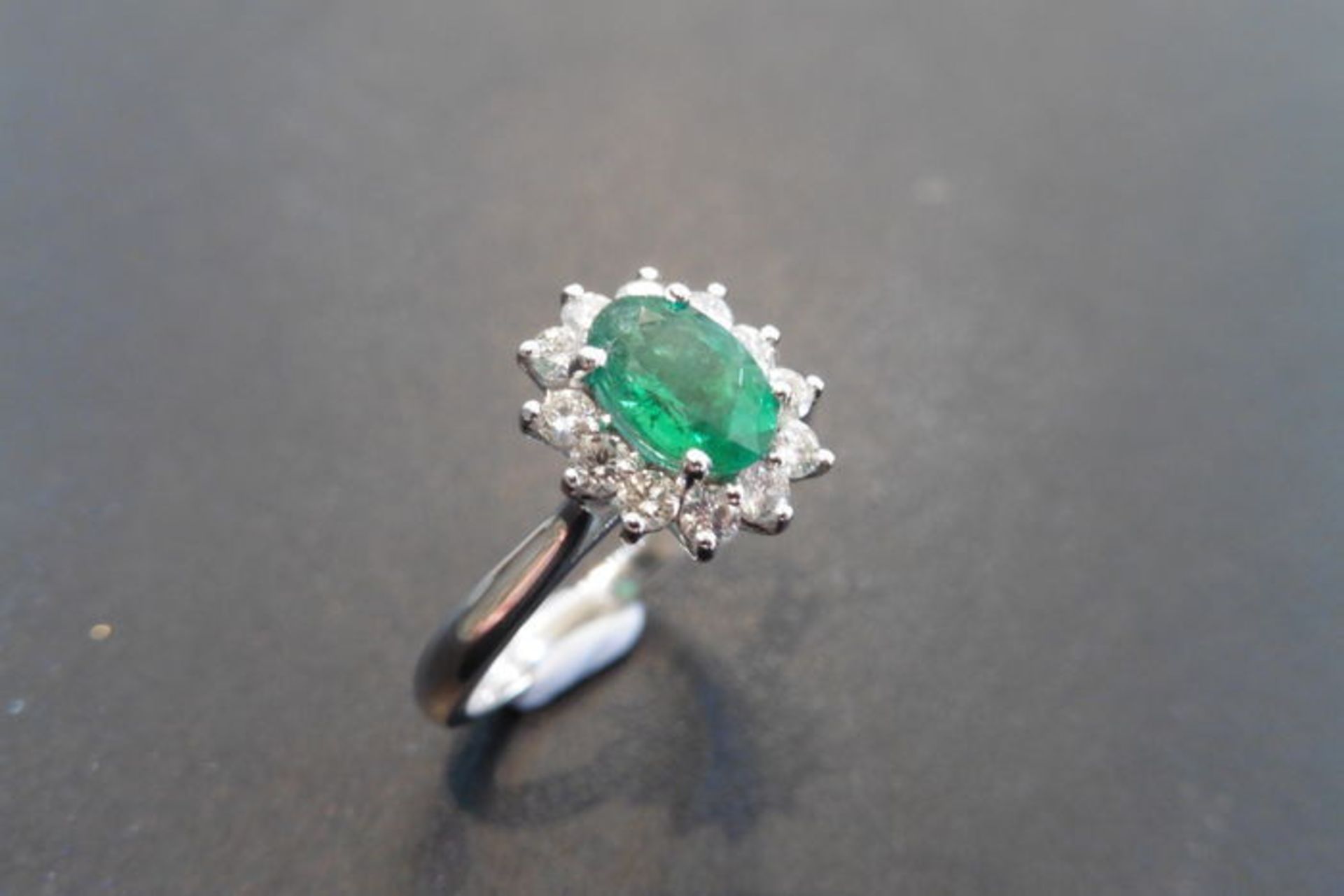 0.80ct emerald and diamond cluster ring set with a oval cut( treated) emerald which is surrounded by