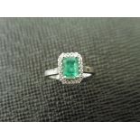 Emerald and diamond ring. Rectangular cut emerald ( treated ) 0.70ct with a halo setting of small