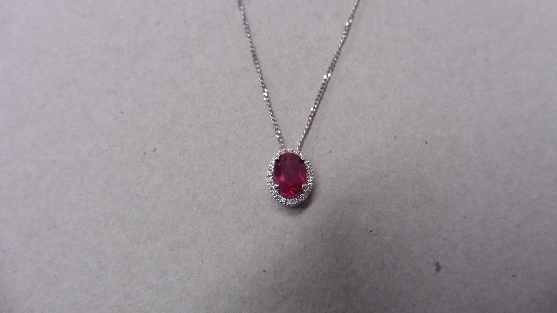 0.80ct ruby and diamond pendant. 7 x5mmoval cut ( glass filled ) ruby with a halo setting of small