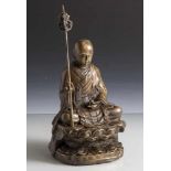 Figurine, Buddha, Bronze, auf Lotussockel sitzend in ornamental verziertem Umhang, einen Stab
