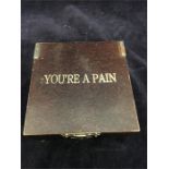 A novelty wooden box with 'You're a Pain' on the fron t and a brass pill box with Aspirin engraved