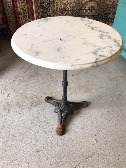 A cast iron tripod table with circular bevelled white marble top