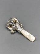 A silver babies rattle with mother of pearl handle