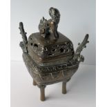 An Oriental brass incense burner with lid on four legs decorated with carved lappets and applied