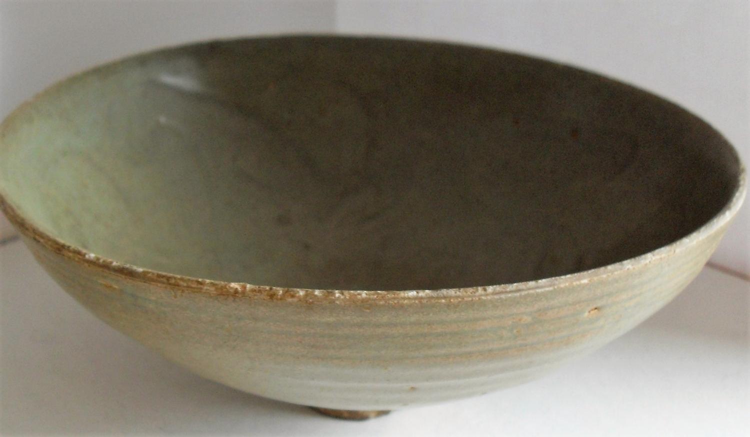 A Chinese Song Dynasty Thanh Hoa celadon bowl on single foot with internal incised scrolling design