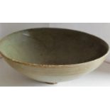A Chinese Song Dynasty Thanh Hoa celadon bowl on single foot with internal incised scrolling design