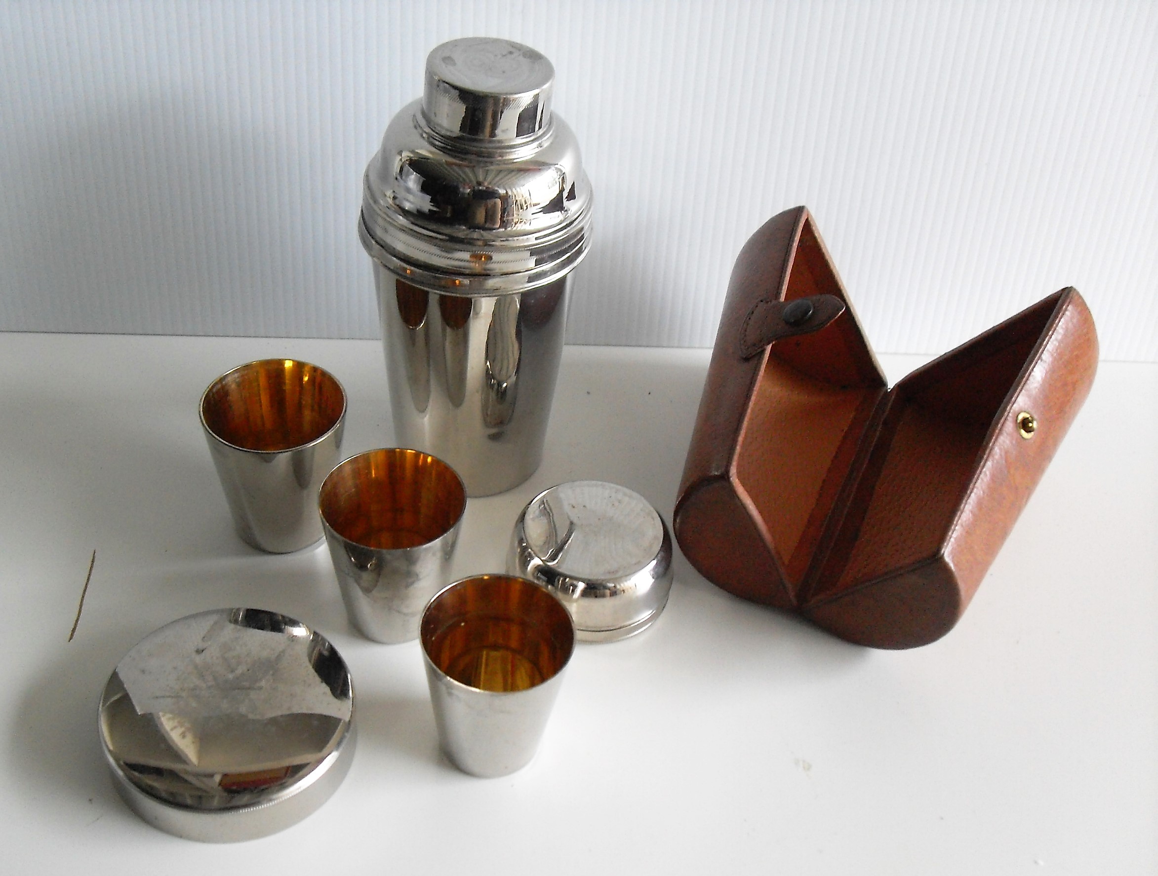 A vintage silver plated cocktail shaker in leather case with three beakers/tots and lid strainer