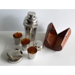 A vintage silver plated cocktail shaker in leather case with three beakers/tots and lid strainer