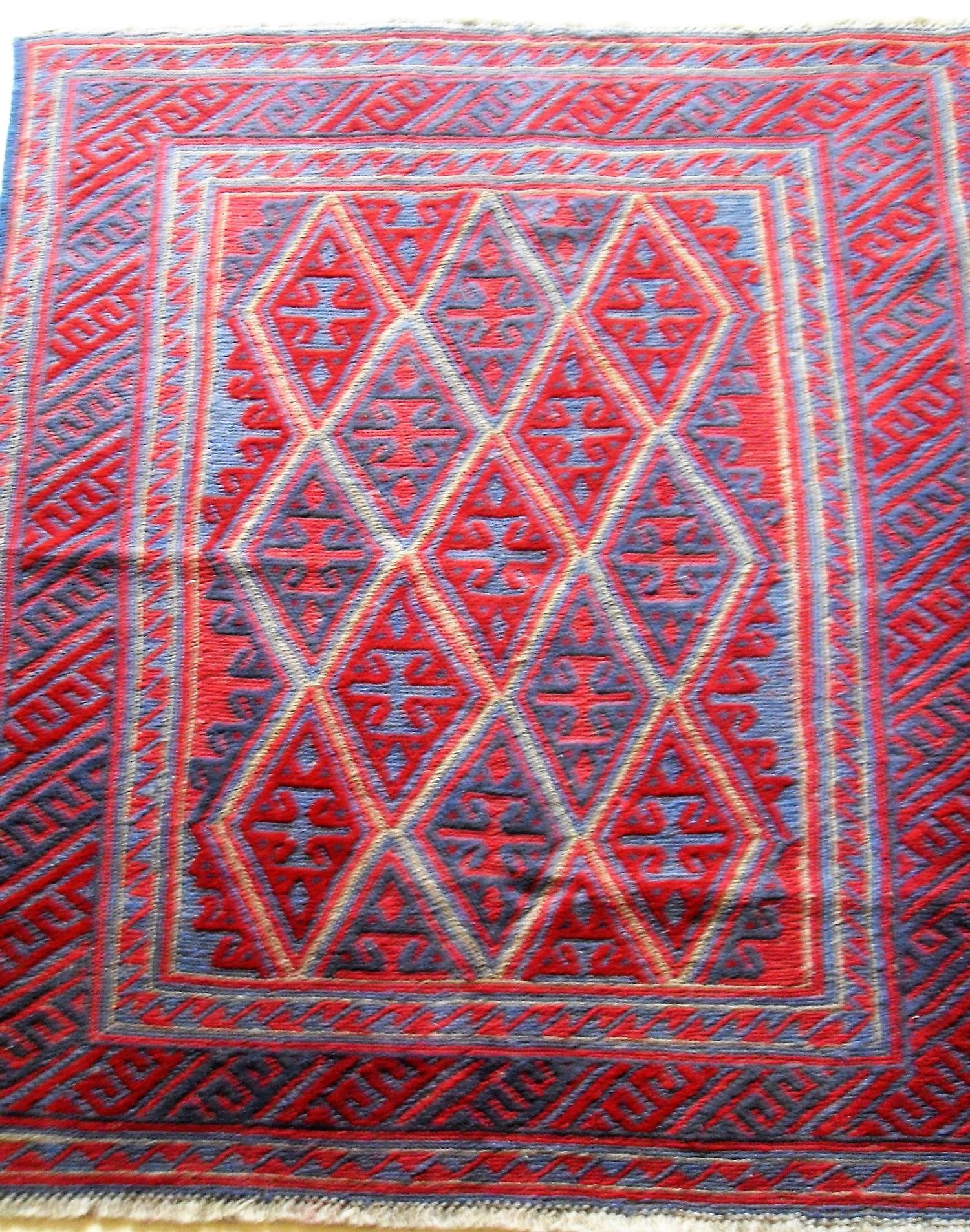 A hand-knotted Afghan tribal Kazak burgundy-ground wool rug with lozenge shapes to centre, double