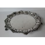 A George V silver salver with pie crust border and anthemion decoration on three claw and ball feet