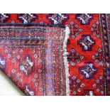 An Afghan hand-knotted Balochi scarlet-ground wool rug with multi-coloured lozenge designs, double